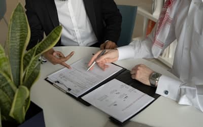 Two men sitting at a table with papers and a pen